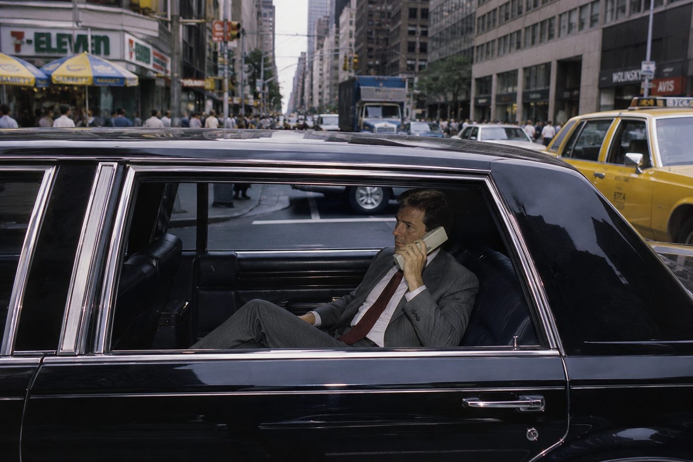 A man takes a call from the back of a sedan on a city avenue